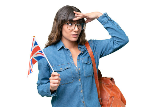 Young caucasian woman holding an United Kingdom flag over isolated background doing surprise gesture while looking to the side