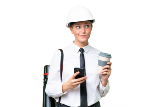 Young architect caucasian woman with helmet and holding blueprints over isolated background holding coffee to take away and a mobile while thinking something