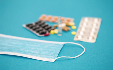 A variety of pills and a protective face mask on a blue background.
