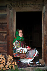Ukrainian girl in national Hutsul clothes with an apple in her hands sits on the threshold of an...