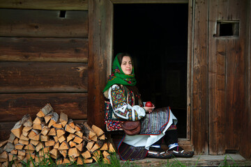 Ukrainian girl in national Hutsul clothes with an apple in her hands sits on the threshold of an...