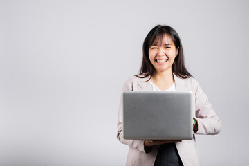 Fototapeta premium Woman smiling confident smiling holding using laptop computer and typing keyboard for online sending email or chat, Portrait excited happy Asian young female studio shot isolated on white background