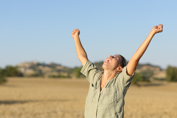 Excited woman raising arms in a field