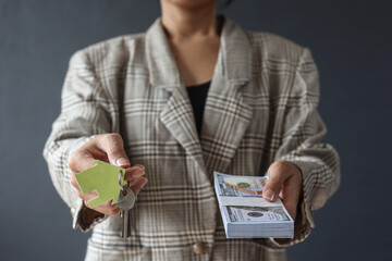 Selling real estate concept with a woman handing house key and money isolated over dark grey background