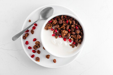 Healthy breakfast. Bowl of greek yogurt with chocolate oat granola and pomegranate seeds on white marble table