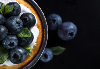 Blueberry tart with fresh berries, flat lay. Homemade cake with blueberries at black background, top view.