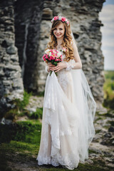 Obraz na płótnie Canvas Young beautiful girl in elegant dress is standing and holding hand bouquet of pastel pink flowers and greens at nature. The bride holds a wedding bouquet outdoors.