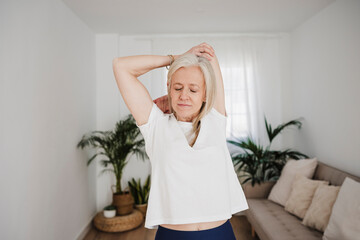 Mature woman stretching arms and exercising at home