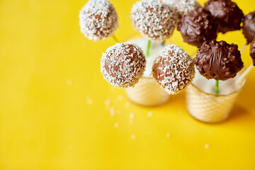 Delicious homemade popcake coconut and dark chocolate cake pops on a yellow background, festival desserts, tasty food