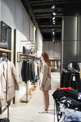 Beautiful woman is wearing protective face mask in shopping center. Girl trying on clothes. Concept of virus protection. Fashion, beauty and shopping concept.