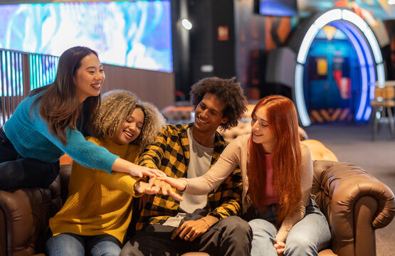 Multiracial friends stacking hands in bowling alley