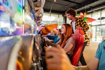 Happy friends having fun playing racing video game at arcade