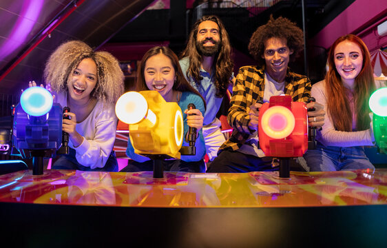 Multiracial friends playing video game in amusement arcade