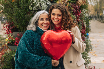 Happy granddaughter and grandmother holding red heart shaped balloon