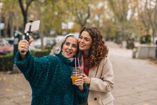 Happy grandmother and granddaughter taking selfie with glass of juice