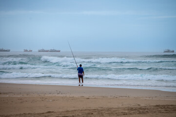 Rear view of man seen fishing along coast