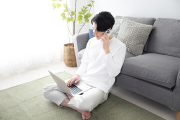 パソコンで何かを調べてスマホでお問い合わせする男性...