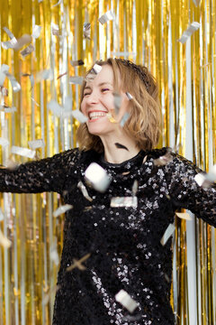 Happy woman wearing black dress under falling confetti in new year's party