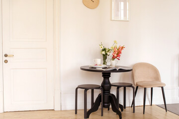 Bouquets of fresh flowers and open magazine placed on table near clean dishware against beige wall small dining room kitchen