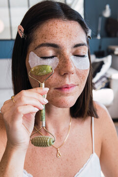 Woman with under eye patches massaging using jade stone roller on face at home