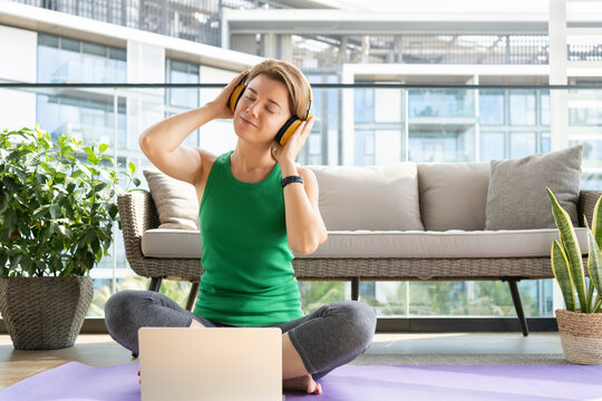 Smiling woman wearing headphones listening to music sitting on balcony