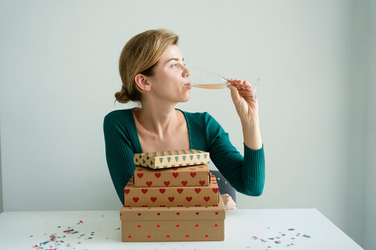 Woman Drinking Champagne On Table With Stack Of Gifts