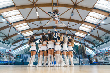 Full shot of a cheerleading squad hrowin one of their teammates high up in the air. Sport concept....