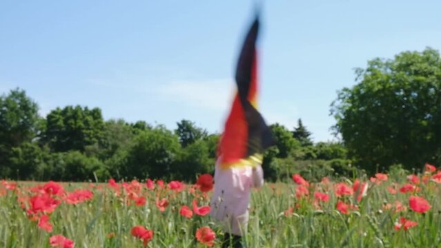 A little blond girl with a Germany flag on her hands on a green wheat field with poppies