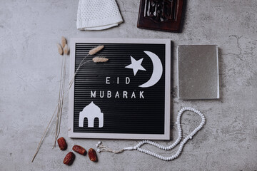 Eid mubarak word on letterboard arrange with islamic ornaments and muslim prayer equipment on gray background. 