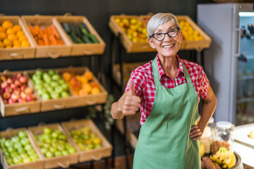 Mature woman works in fruits and vegetables shop. Portrait of small business supermarket owner.