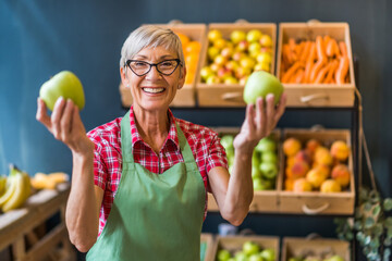 Worker in fruits and vegetables shop is holding apples.