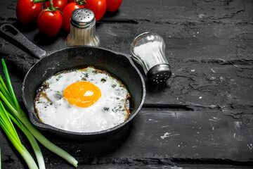 Fried eggs in a pan with green onions and tomatoes.