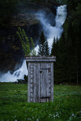 Traditional wooden toilet house on a pasture right in front of waterfall Huldefossen in Norway