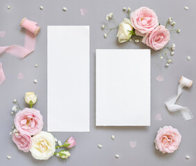Blank paper cards between pink roses and pink silk ribbons on grey top view, wedding mockup