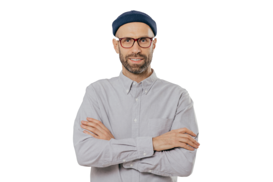 Horizontal shot of satisfied self confident male designer wears stylish headgear, dressed in white shirt, keeps arms folded, has dark stubble, isolated over white background. People and style concept