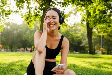 Young asian woman using cellphone and headphones on yoga mat in park