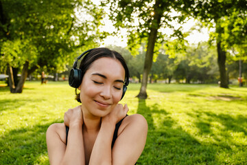 Young asian woman with headphones smiling during workout in park