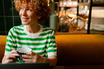 Mid white woman with curly hair smiling and drinking coffee in cafe
