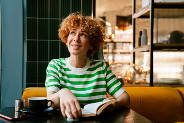 Mid white woman with curly hair reading book while sitting in cafe