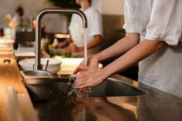 Young chef woman washing hands while working in restaurant kitchen