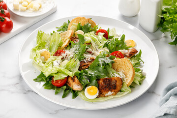 Caesar salad with roasted chicken meat, tomatoes, croutons and parmesan cheese in white plate.