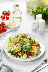 Caesar salad with roasted chicken meat, tomatoes, croutons and parmesan cheese in white plate.