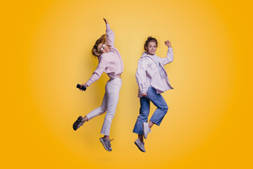 Portrait of two joyful young woman jumping and celebrating over yellow background.