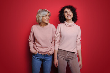 Portrait of two happy women smiling while standing over red background. Smile emotions. Looking camera. Fashion lady. Happy people positive emotions.