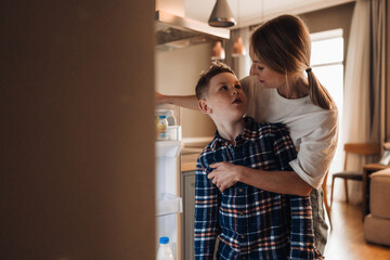 Young mother standing with her little son near fridge in kitchen