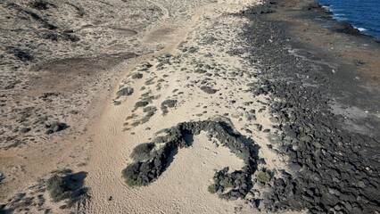 Spain, Lanzarote, Canary , Charco del Palo is a naturist village in the north of the island - drone aerial view of expanses of sand, black rocks black cliffs of volcanic lava origin and the ocean sea 