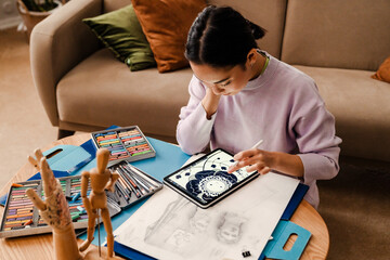 Young asian woman drawing on digital tablet while sitting at table