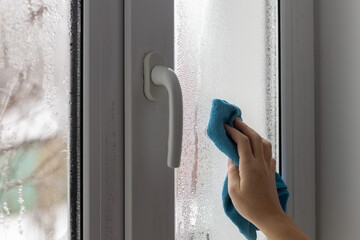 A womans hand wipes the condensate from the window glass.
