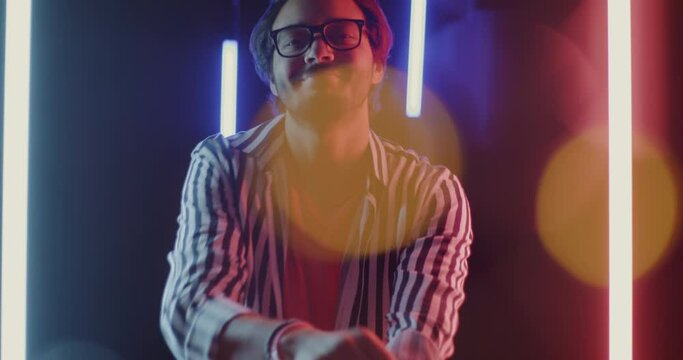 Portrait of Middle Eastern man pointing at camera and dancing in dark space with neon lamps illumination. Nightlife and millennials concept.