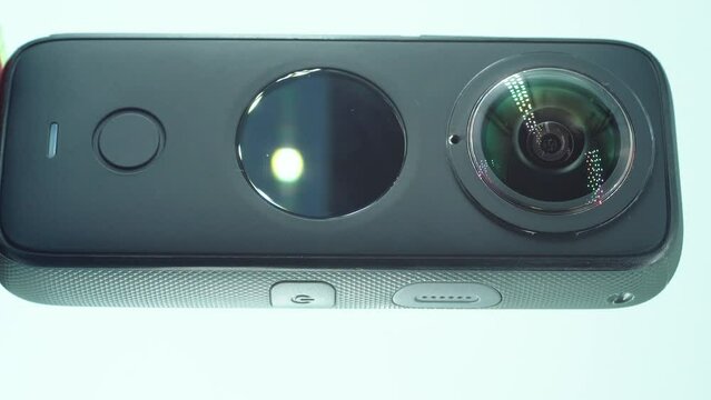A close up vertical shot of a 360 camera with dual lens, two lens covers, shiny studio lighting reflecting, round screen, function button, on a rotating stand, slow motion, 4K video